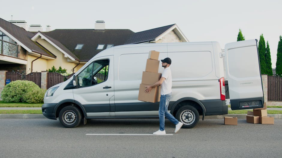 Two movers from Man with Van Putney are engaged in a home relocation, standing behind an open van with its back doors wide open on a paved street. They are lifting and loading a large, rectangular pie